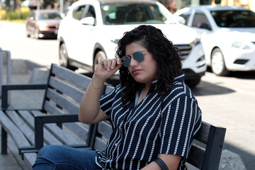 Mujer en la calle sentada en una banca con lentes de sol