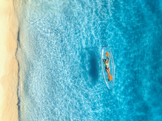 Aerial view of young woman lying on transparent canoe in blue sea at sunset. Summer in Zanzibar....