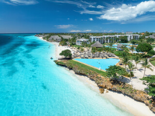 Aerial view of pool, sandy beach, palms, bungalows, blue ocean