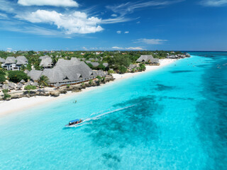 Aerial view of sandy beach, blue sea, bungalows, green palms, umbrellas, floating boat at sunset. Summer travel in Nungwi, Zanzibar island. Tropical landscape. Top drone view of luxury resort. Ocean