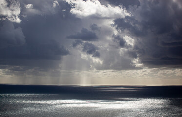 Overcast grey sky with low textured clouds. Sunlight peeks through the clouds and falls on the sea. Background. Horizontal