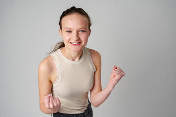 Young Woman in Casual Attire Smiling and Making a Fist Pump Gesture on a Plain Background