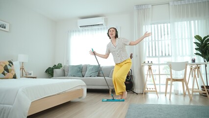 Smiling housekeeper with headphone listen music while cleaning floor. Happy smart caucasian mother mopping floor while dancing and singing to lively song at living room. Mom doing housework. Pedagogy