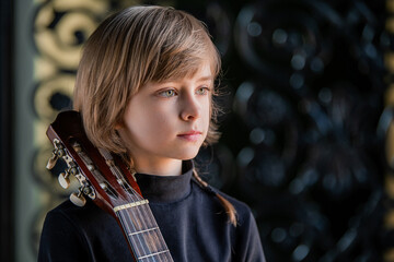 A young boy sits on a stool and plays the guitar.