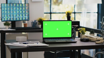 Focus on isolated screen laptop on company desk with computer desktop in blurry background showing stock exchange data. Chroma key notebook and trading platform displayed on PC screen in the back