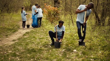 African american volunteers team digging holes and planting trees in a forest, doing litter cleanup and putting seedlings in the ground for nature cultivation concept. Conservation project. Camera B.