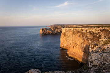 Landscape photo of dramatic, steep orange cliffs by the atlantic at sunset. Shot in Farol fo Cabo de Sao Vincente near Sagres, Portugal.