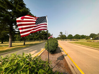 American Flag Waves at the entrance to a cemetery. Park-like setting in the background of view....