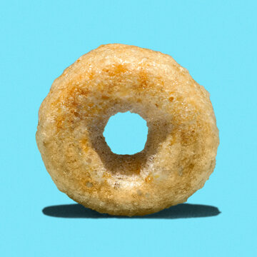 Single honey cheerios cereal isolated on blue. Close-up macro detail.