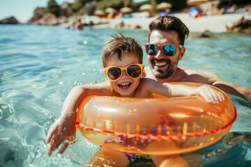 Father and son in sunglasses with inflatable ring at beach, having fun on summer vacation