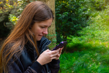 mujer joven con mirando su celular en la naturaleza. chica enviando mensajes con su celular con...