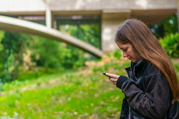 mujer joven con mirando su celular en la naturaleza. chica enviando mensajes con su celular con...