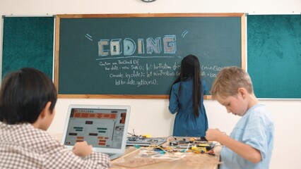 Asian boy coding program while caucasian friend fixing electric board at STEM class. Energetic...