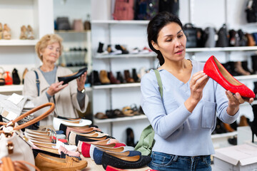 Asian woman selecting new shoews while standing in salesroom shoeshop. Elderly European woman...