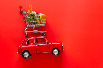 Delivery of products. Red car with a shopping basket with fruits and vegetables on a red...