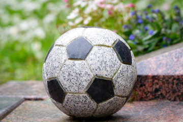 a stone football as decoration on a grave in front of colourful flowers in a blurred background
