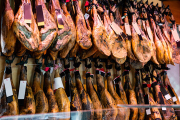 Abundance of dry-cured pig's legs in spanish jamoneria. Lots of preserved pork meat at counter in...