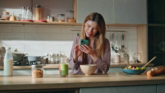 Housewife messaging cellphone kitchen at weekend morning. Woman looking phone