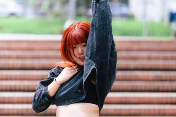Korean woman with red hair dancing carefree, embracing the rhythm in an urban outdoor area