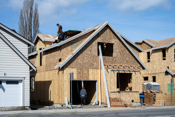 Workmen on a new residential community construction job site, house shells ready for roofing and...