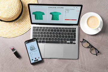 Online store website on laptop screen. Computer, smartphone, coffee and accessories on grey table,...