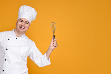Naklejka premium Portrait of happy confectioner in uniform holding whisk on orange background, space for text