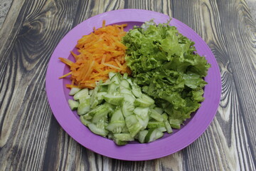 Fresh carrots, cucumber, and lettuce all cut up for a healthy vegetable salad.