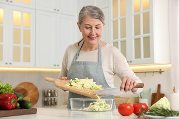 Happy housewife putting cut cabbage into glass container at white marble table in kitchen