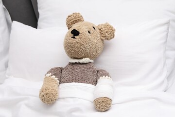 Toy cute bear with bandage under blanket in bed