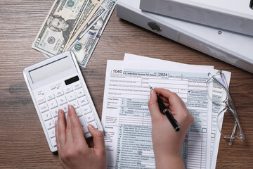 Payroll. Woman using calculator while working with tax return forms at wooden table, top view