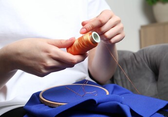 Woman with spool of thread embroidering on cloth at home, closeup