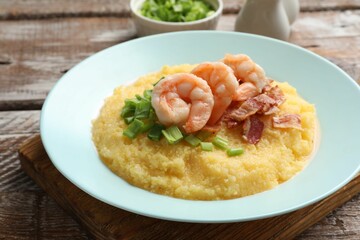 Plate with fresh tasty shrimps, bacon, grits and green onion on wooden table, closeup