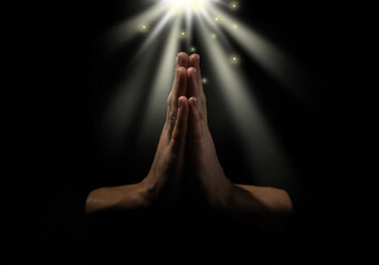 Christian woman holding hands clasped under holy light in darkness, closeup. Prayer and belief