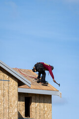 Workman with hammer working on roof of new home construction, minimalist image on a sunny spring day
