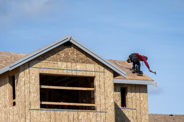 Workman with hammer working on roof of new home construction, minimalist image on a sunny spring...