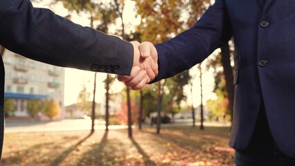 Business woman shaking hands with partner, outdoors. Businessmen in suits greet on street with hand...