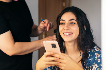 Young Spanish woman using smartphone in a hair and makeup treatment
