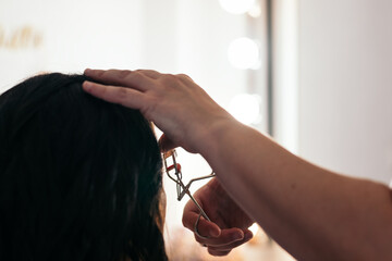 Close-up of a beautician curling the eyelashes of an unrecognizable woman in a makeup studio