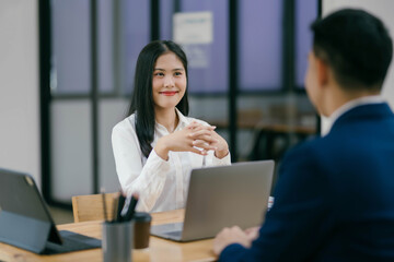 A woman and a man are sitting at a table with laptops in front of them