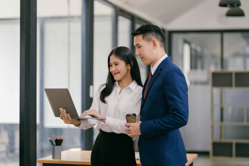 A woman and a man are standing in front of a laptop, looking at it