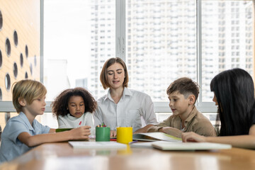 Teacher is teaching student about lesson from the books in the classroom, the children are happy. Some ask teacher, a boy in blue shirt is reading a book on his own and a girl is drawing. Erudition.