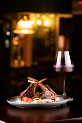 grilled rack of lamb with potatoes paired with glass of red wine on wooden table in close-up