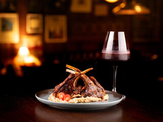 grilled rack of lamb with potato compote paired with glass of red wine on wooden table in pub