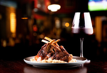 grilled rack of lamb with potatoes paired with glass of red wine on blurred pub background