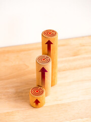 Target icons and rise arrows on round wooden sticks as business graph steps isolated on wood desk on white background. Business growth graph process, goal, success, and economic improvement concepts.