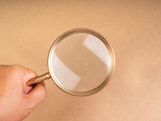 Researching, analysis, content idea searching, creative inspiration and find keywords concepts. Close-up gold empty magnifying glass in businessman hand holding on brown recycle paper background.