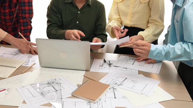 Smart architect and safety engineer discussion about building plan on table with architectural document, measurement tools and wooden block scatter around at modern office. Closeup. Delineation.