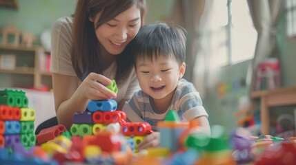 Fototapeta premium Asian young boy is playing with a stack of colorful blocks while his mother watches.