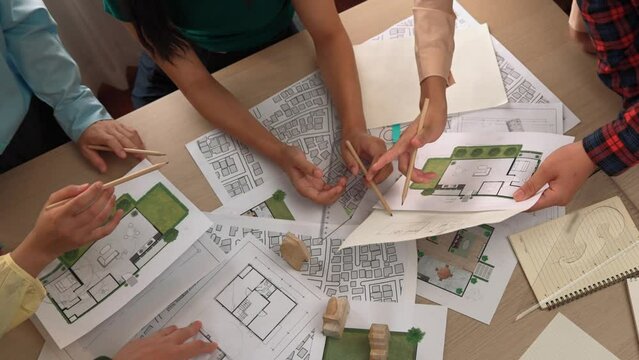 Smart architect and safety engineer discussion about building blueprint on table with architectural document, measurement tools and wooden block scatter around at modern office. Closeup. Delineation.
