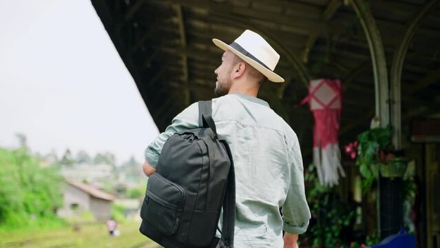 Solo traveler in straw, denim shirt explores authentic Haputale rail station with backpack, camera in hand. Station vibrant with travelers, local culture. Man walks along platform, adventure. Slowmo